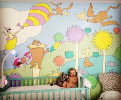 a baby sitting in a crib with dr seuss mural on the wall behind it