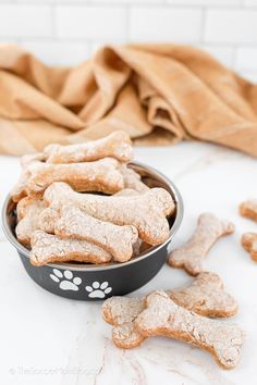 a bowl full of dog treats next to a pile of bone shaped cookies on a table