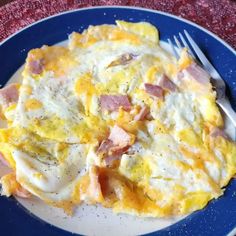 an omelet with ham and cheese on a blue plate next to a fork