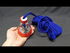 a hand holding a blue rope with a red bottle in it on a black surface