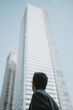 a man standing in front of a tall building with his back to the camera looking up