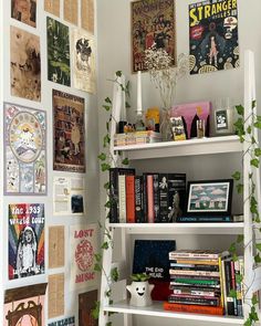 a bookshelf filled with lots of books next to a wall covered in posters