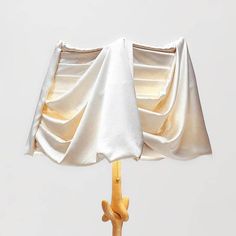 an umbrella with white fabric draped over it on a wooden stick in front of a gray sky