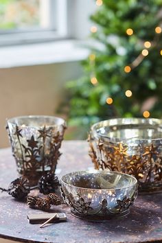 three metal bowls sitting on top of a table next to a christmas tree with lights in the background