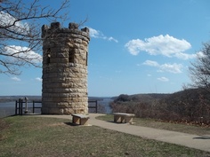 a stone tower sitting on top of a lush green field next to a lake and trees