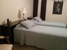 two twin beds in a hotel room with blue sheets and pillows on them, one has a chair next to it