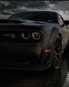 the front end of a black sports car on a wet road with dark clouds in the background