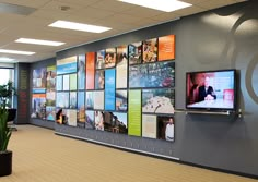 a wall with many pictures on it and people walking in the hallway next to it