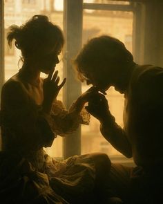 two people sitting next to each other in front of a window with their hands together