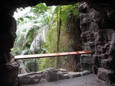 a wooden bench sitting in the middle of a forest filled with trees and rocks on either side of a stone wall