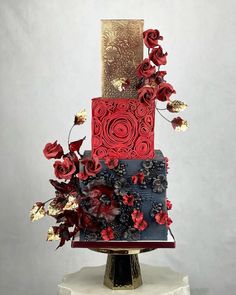 a three tiered cake with red flowers and gold decorations on it's side