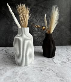 two black and white vases with dried plants in them sitting on a marble surface