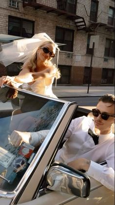 a man and woman sitting in the back of a white convertible car on a city street