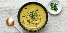 a bowl of hummus next to a spoon on a white tablecloth with green herbs