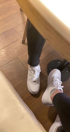 a person wearing white tennis shoes standing next to a skateboard on a wooden floor