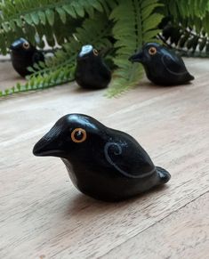 small black birds sitting on top of a wooden floor next to ferns and fern leaves