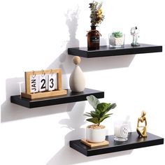 two black floating shelves with calendars, plants and other decorative items on each shelf