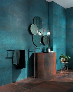 a bathroom with blue walls and brown flooring is pictured in this image, there are three round mirrors on the wall