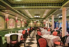 a dining room with checkered flooring and green walls, white tablecloths and pink upholstered chairs