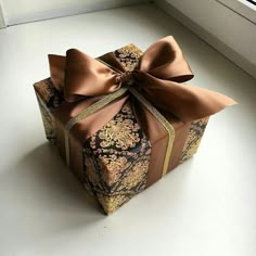 a brown and gold gift box with a bow on it's side sitting in front of a window