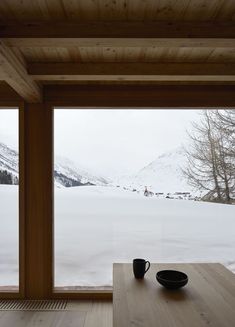 a table with two cups on it in front of a window overlooking snow covered mountains