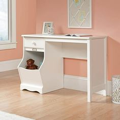 a white desk with a stuffed animal in the bottom drawer and pink walls behind it