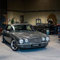 a grey car parked in a garage next to other cars and people working on machines