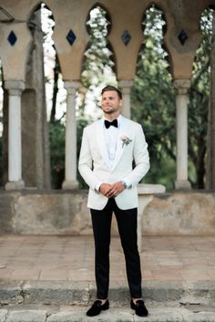 a man in a white tuxedo and black bow tie standing on some steps