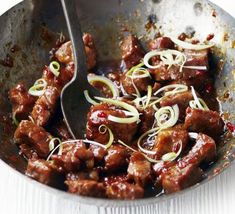 meat and onions are being cooked in a skillet with a spoon on the side