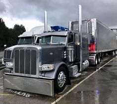 two semi trucks parked in a parking lot on a rainy day with dark clouds overhead