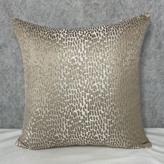 a pillow that is sitting on top of a white bed sheet with silver and gold print