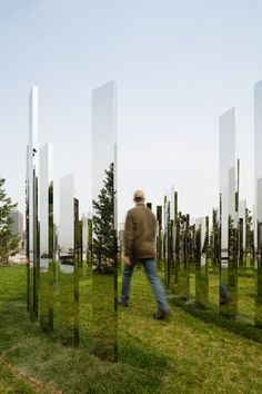 a man is walking in the grass near some tall glass sculptures that look like trees