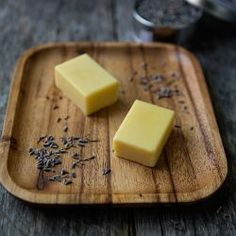 two pieces of butter on a wooden cutting board with seeds and seasoning in the background