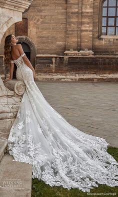 a woman in a wedding dress leaning against a stone wall with her back to the camera