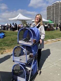 a woman pushing a blue stroller with her dog in it at an outdoor event