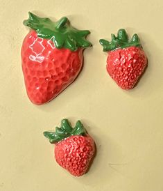 three ceramic strawberries are sitting on a table top, one is red and the other is green