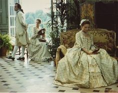 three people in period dress sitting on old fashioned chairs and looking at something off to the side