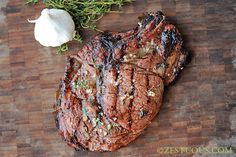 two steaks on a cutting board with garlic and herbs