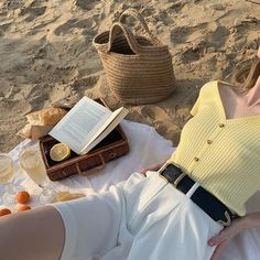 a woman laying on the beach with her purse and book