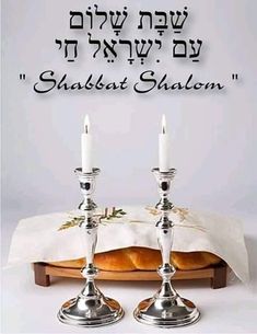 two silver candles sitting on top of a table next to a white cloth with the words shabbat shallom