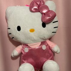 a hello kitty stuffed animal sitting on top of a pink sheeted wall with a bow in it's hair