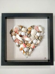 a heart made out of seashells in a black frame on a white wall