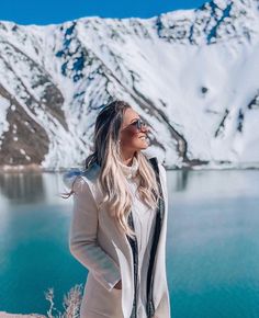 a woman standing on top of a snow covered mountain next to a body of water