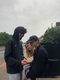 two people standing next to each other near a trash can on the side of the road