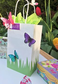 a paper bag with butterflies on it sitting on a table next to some boxes and flowers