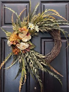 a wreath is hanging on the front door with dried flowers and foliages around it