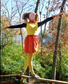 a woman in yellow and red is balancing on a wooden platform with her arms outstretched