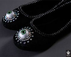 pair of black slippers with green eyes and pearls on the bottom, sitting on a dark surface