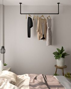 a bedroom with clothes hanging on the wall and a bed in the foreground, next to a potted plant