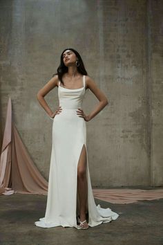 a woman standing in front of a wall wearing a white dress and high slit skirt